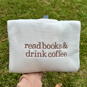 May include: A white sweatshirt with the text "read books & drink coffee" embroidered in brown on the front.