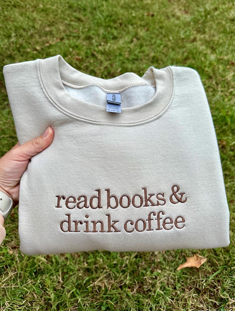 May include: A beige sweatshirt with the text "read books & drink coffee" embroidered in brown on the front.