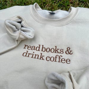 May include: A beige sweatshirt with the text "read books & drink coffee" embroidered in brown on the front.
