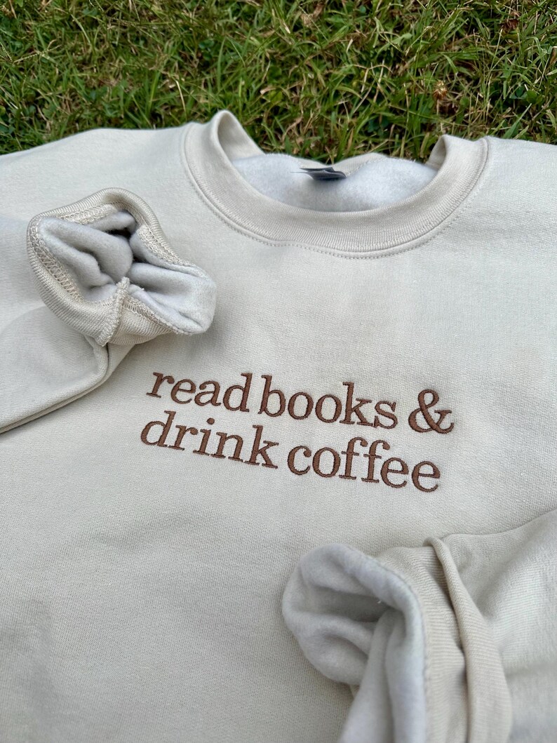 May include: A beige sweatshirt with the text "read books & drink coffee" embroidered in brown on the front.