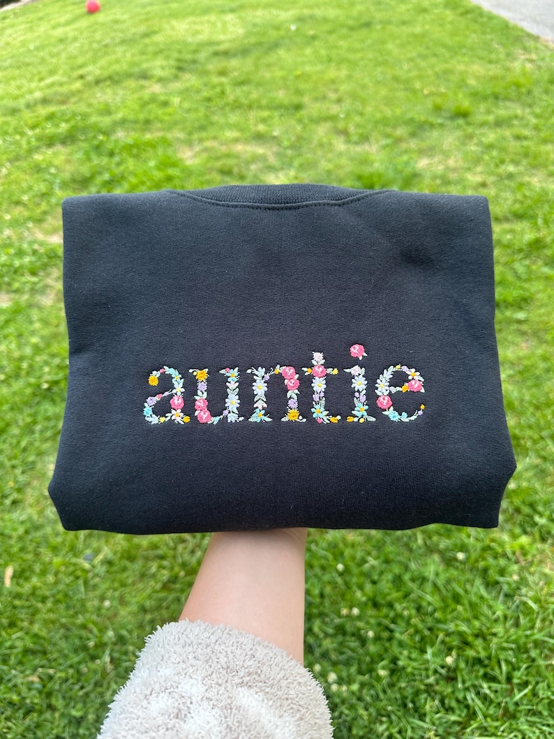 K&ouml;nnte beinhalten: Schwarzer Pullover mit dem Wort "auntie" in bunten Blumen gestickt.