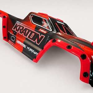 Puede incluir: Carrocería de coche RC Kraton Mini roja, negra y blanca. El cuerpo presenta el texto "KRATON" en letras blancas grandes, junto con el logotipo "ASRMA HORIZON". La carrocería tiene un acabado brillante y está diseñada para un vehículo de radiocontrol a pequeña escala.