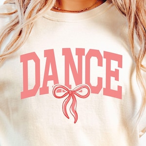 May include: A white t-shirt with the word "DANCE" in pink letters with a pink bow underneath.
