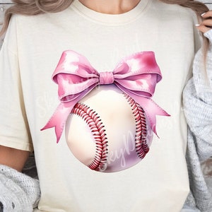 May include: A white baseball with a pink bow on top. The baseball has red stitching and is on a white t-shirt.