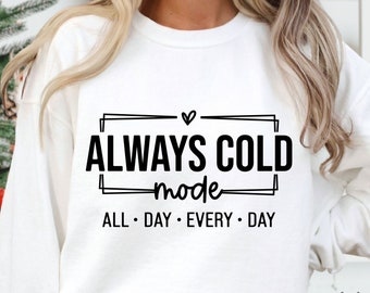May include: White sweatshirt with black text that reads "Always Cold Mode" with a heart symbol above the word "Cold". Below the text is "All Day Every Day".