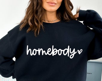 Può includere: Felpa nera con il testo "homebody" in lettere corsive bianche con un piccolo simbolo di cuore.