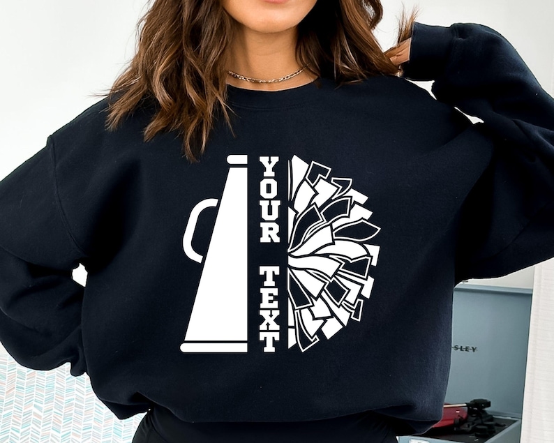 Pu&ograve; includere: Felpa nera con design di megafono e pompon da cheerleader bianchi. Il testo "YOUR TEXT" &egrave; stampato verticalmente. Il design &egrave; in stile grafico audace, ideale per le squadre di cheerleader.