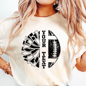 May include: White t-shirt with a black and white graphic design of a football and a cheerleading pom-pom. The text "YOUR TEXT" is printed vertically on the shirt.