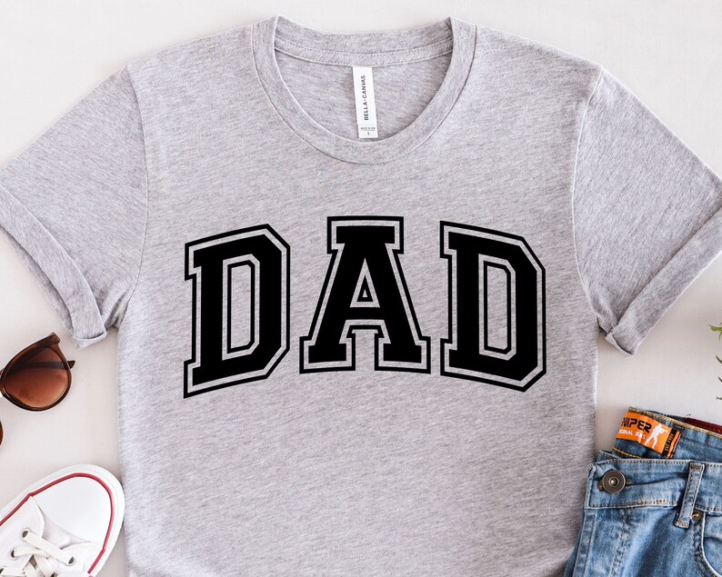 Op de afbeelding: Een grijs T-shirt met het woord "DAD" in zwarte blokletters.