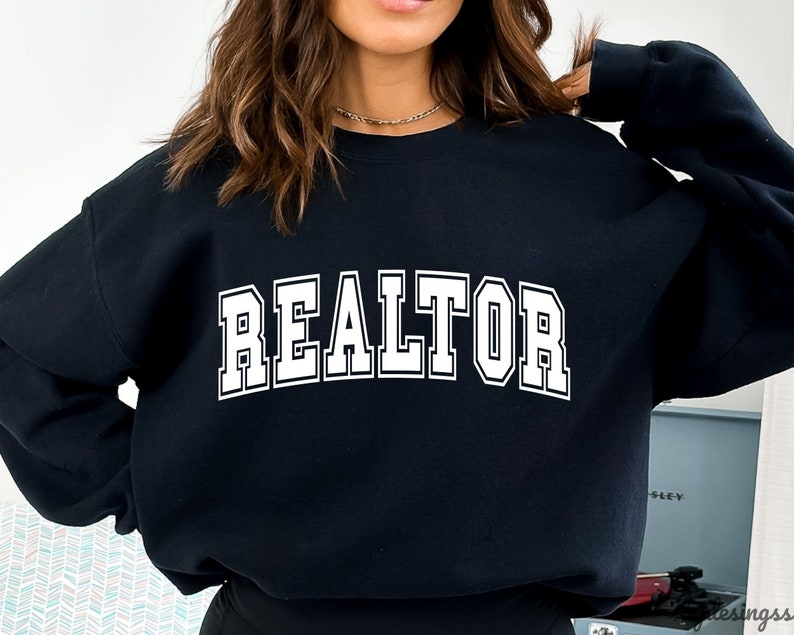 May include: Black sweatshirt with the word "REALTOR" printed in white on the front.