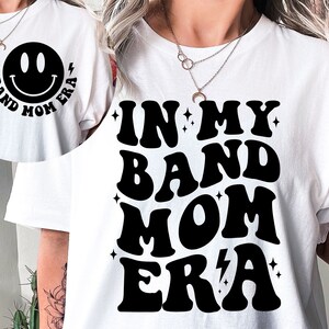 Pu&ograve; includere: Maglietta bianca con testo nero che recita "In My Band Mom Era" in un font retr&ograve;. Un'emoticon con le parole "Band Mom Era" sono stampate sul retro della maglietta.