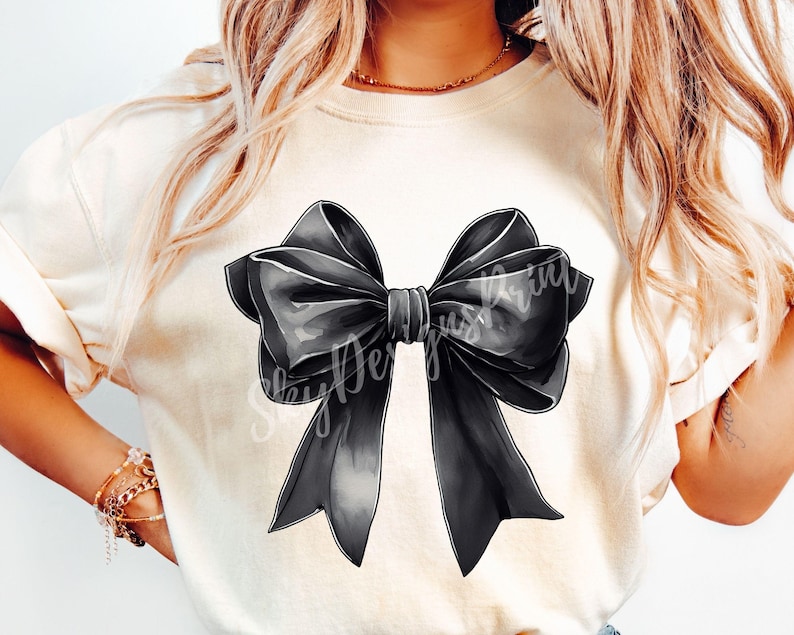 May include: A white t-shirt with a large black bow graphic. The bow is drawn in a watercolor style with soft edges.