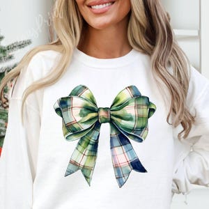 Peut inclure: Sweat-shirt blanc orn&eacute; d'un grand n&oelig;ud aquarelle. Le n&oelig;ud pr&eacute;sente un motif &agrave; carreaux dans les tons de vert, de bleu et de rose. Le motif est centr&eacute; sur le devant du haut &agrave; manches longues, cr&eacute;ant un look festif et &eacute;l&eacute;gant.