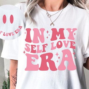May include: White t-shirt with a pink and red graphic that says "In My Self Love Era".