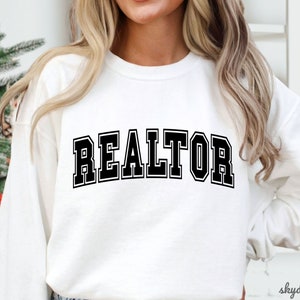 May include: White sweatshirt with black text that reads "REALTOR" in a varsity style font.