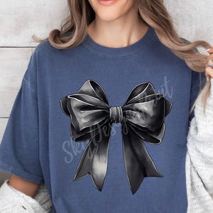 May include: A dark blue t-shirt with a large black bow graphic on the front. The bow is drawn in a realistic style with shading and highlights.