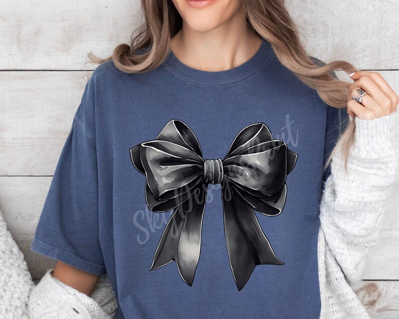 May include: A dark blue t-shirt with a large black bow graphic on the front. The bow is drawn in a realistic style with shading and highlights.