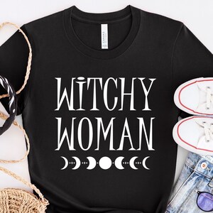 May include: Black t-shirt with white text that reads "Witchy Woman" and a row of white crescent moons.