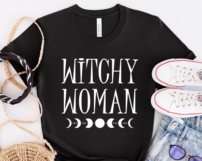 May include: Black t-shirt with white text that reads "Witchy Woman" and a row of white crescent moons.