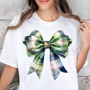Peut inclure: T-shirt blanc avec un grand n&oelig;ud aquarelle. Le n&oelig;ud pr&eacute;sente un motif &agrave; carreaux dans des tons de vert, de bleu et de rose. Le design est centr&eacute; sur le t-shirt, cr&eacute;ant un look simple mais accrocheur.