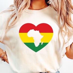 May include: A white t-shirt with a red, yellow and green heart-shaped design featuring an outline of the continent of Africa.