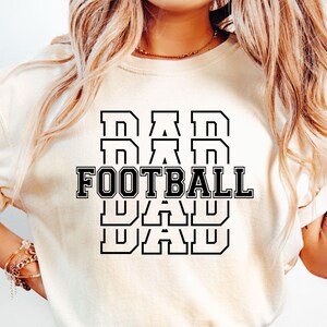 May include: White t-shirt with black text that reads "DAD FOOTBALL DAD DAD" in a stacked, bold font.