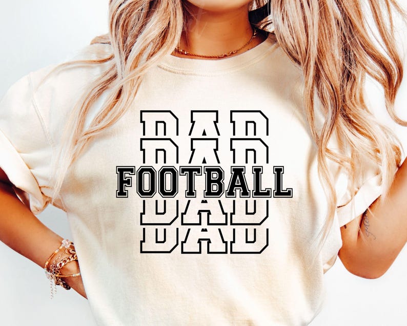 May include: White t-shirt with black text that reads "DAD FOOTBALL DAD DAD" in a stacked, bold font.