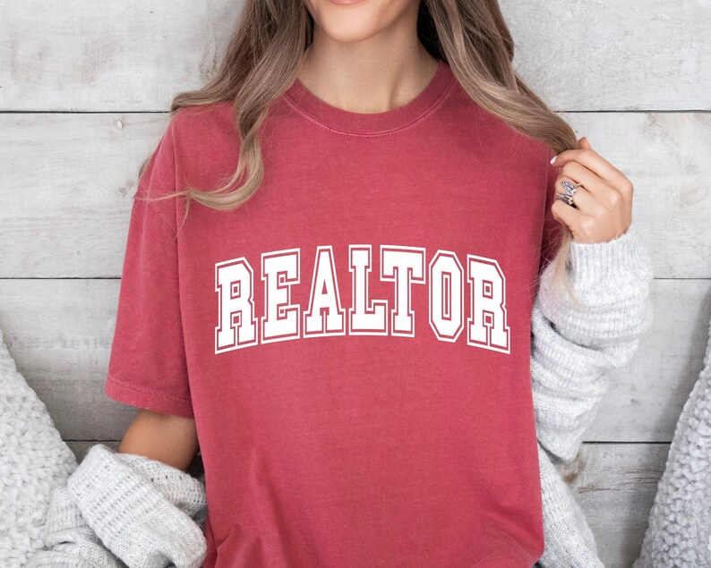 May include: A red t-shirt with the word "REALTOR" printed in white on the front. The shirt has a vintage, distressed look.