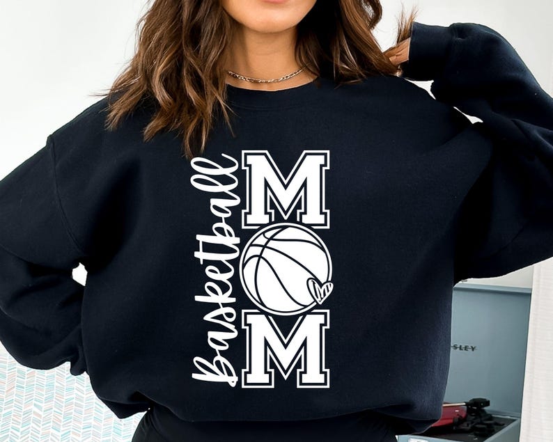 Może przedstawiać: Czarna bluza z białym napisem "Basketball Mom" z grafiką koszyk&oacute;wki i serca.