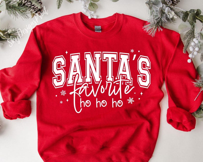 May include: A red sweatshirt with the text "SANTA'S favorite ho ho ho" in white. The text is in a collegiate style font. The sweatshirt has long sleeves and a crew neck.