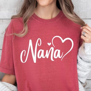 Puede incluir: Una camiseta roja con la palabra "Nana" en letras blancas cursivas y un dise&ntilde;o de coraz&oacute;n blanco.