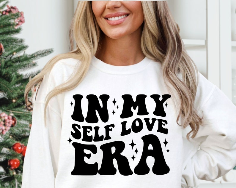 May include: White sweatshirt with black text that reads "In My Self Love Era" in a retro font.