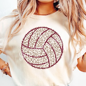 Op de afbeelding: Crèmekleurig T-shirt met een volleybalontwerp. De volleybal heeft een luipaardprintpatroon in bruin- en beigetinten, met bordeauxrode naden. Het shirt is een casual stijl, geschikt voor sportliefhebbers.