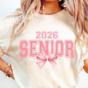 May include: A white t-shirt with the text "2026 SENIOR" in pink letters with a pink bow underneath.