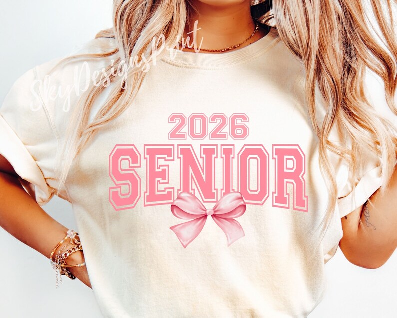 May include: A white t-shirt with the text "2026 SENIOR" in pink letters with a pink bow underneath.