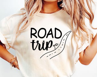 Può includere: Una maglietta bianca con il testo "ROAD trip" in lettere nere e un'illustrazione in bianco e nero di una strada tortuosa con una freccia che punta a destra.