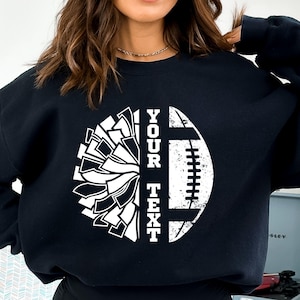 May include: Black sweatshirt with a white graphic of a cheerleading pom-pom and a football with the text "YOUR TEXT".