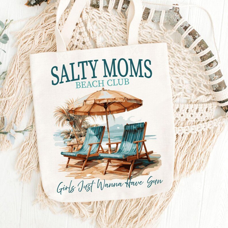 May include: A white canvas tote bag with the text "Salty Moms Beach Club" and an illustration of two beach chairs under an umbrella. The text "Girls Just Wanna Have Sun" is at the bottom of the bag.