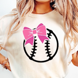 Könnte beinhalten: Ein weißes T-Shirt mit einem schwarzen Baseball-Motiv und einer rosa Schleife oben.