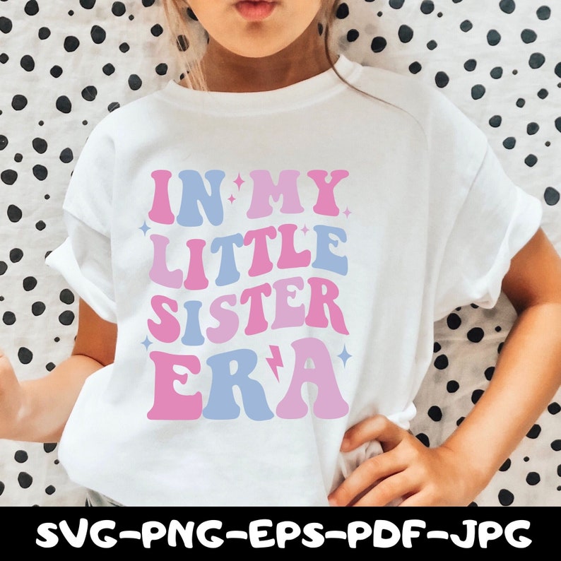 May include: A white t-shirt with a pink and blue graphic that says "In My Little Sister Era" with stars and a lightning bolt.
