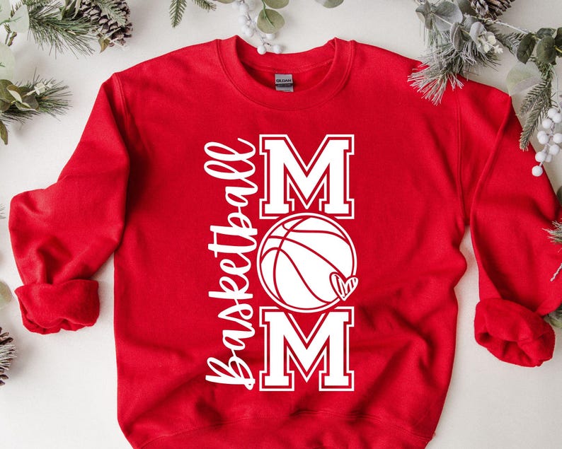 Może przedstawiać: Czerwona bluza z białym napisem "Basketball Mom" z grafiką koszyk&oacute;wki i serca.