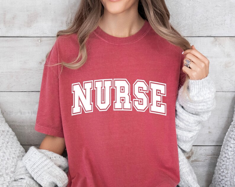 May include: A red t-shirt with the word "NURSE" printed in white letters.