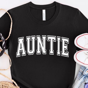 May include: Black t-shirt with white text that reads "AUNTIE" in a varsity style font.