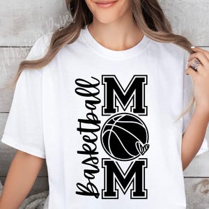 Może przedstawiać: Biała koszulka z czarnym napisem "Basketball Mom" z grafiką koszyk&oacute;wki i serca.