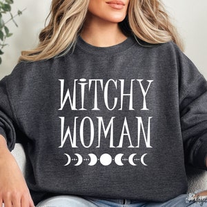 May include: A dark gray sweatshirt with the text "Witchy Woman" in white lettering and a row of white crescent moons below the text.
