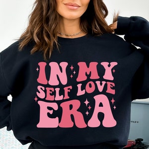 May include: Black sweatshirt with a pink and white graphic that says "In My Self Love Era".