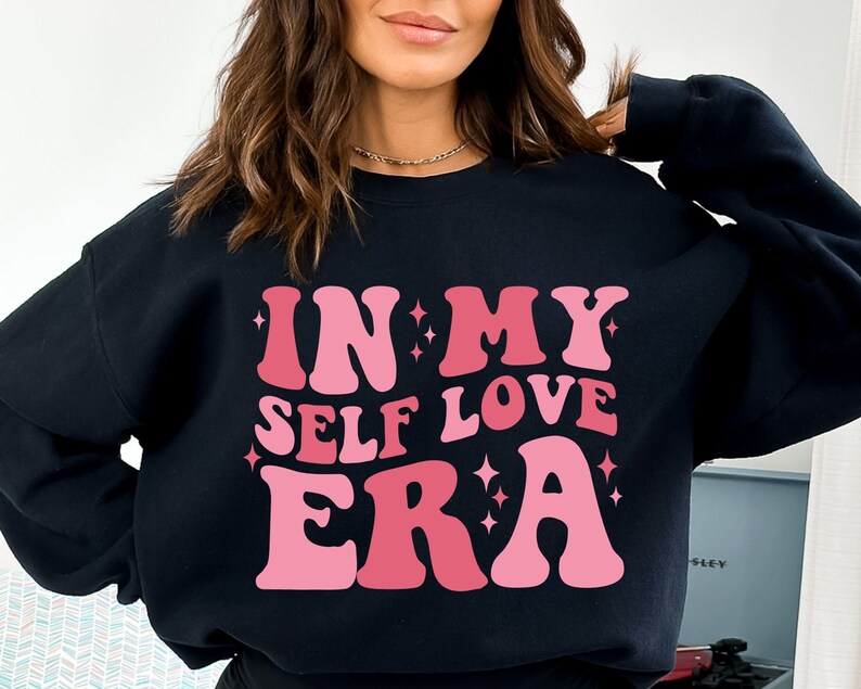 May include: Black sweatshirt with a pink and white graphic that says "In My Self Love Era".
