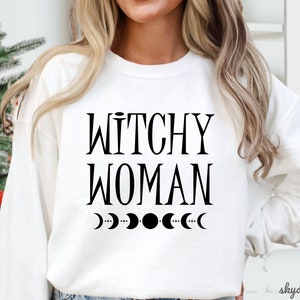 May include: White sweatshirt with the text "Witchy Woman" and a row of crescent moons printed in black.