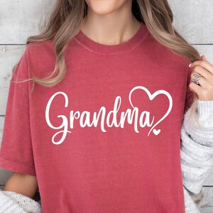 May include: A red t-shirt with the word "Grandma" in white cursive lettering and a white heart design.
