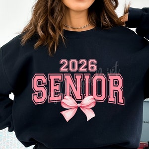 May include: Black sweatshirt with pink text that says "2026 Senior" with a pink bow underneath.